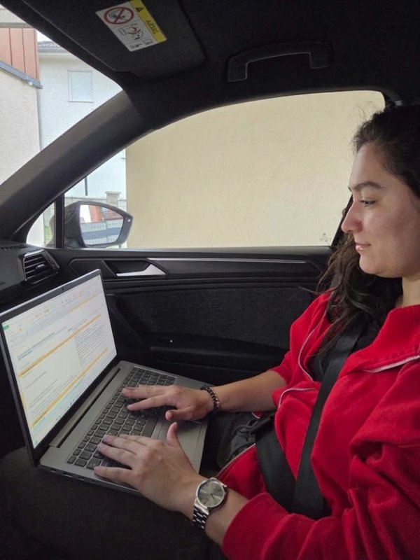 A woman is sitting in the car, working on a laptop.