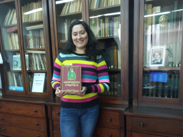 Woman standing in front of a display case with books, holding a book in her hand.