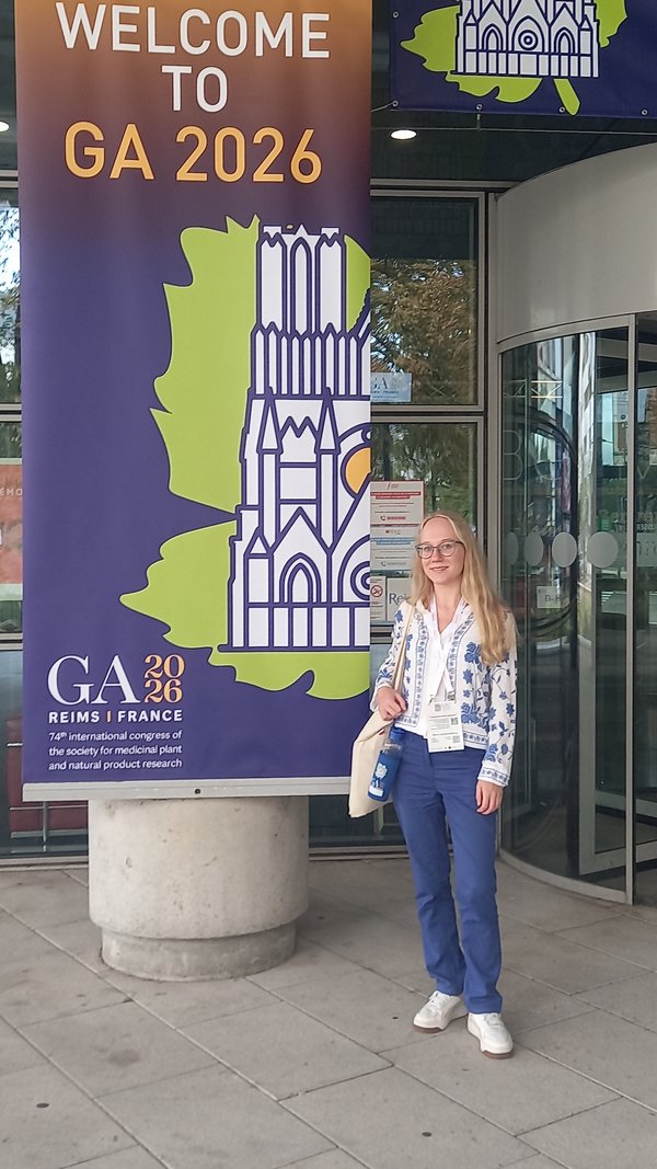 A woman is standing in front of a conference entrance next to an advertising banner.