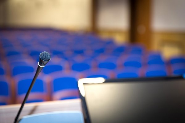 Microphone in the foreground, behind it a conference room with blue chairs.