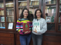 Two women are standing in front of a display case with books, each holding a book in their hands.